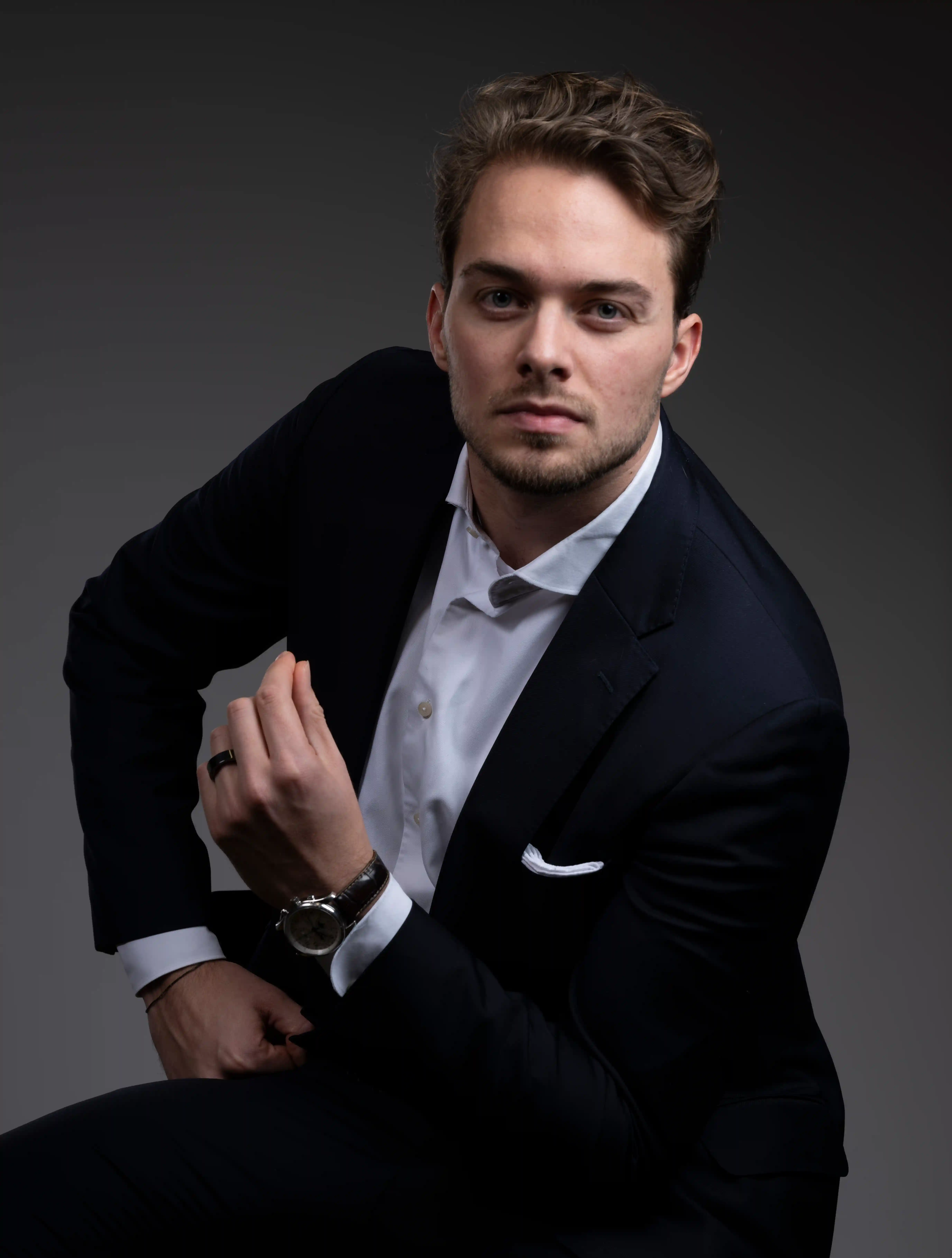 Professionelles Bewerbungsfoto eines jungen Mannes im dunklen Anzug mit weißem Hemd, aufgenommen im Fotostudio vor dunklem Hintergrund.